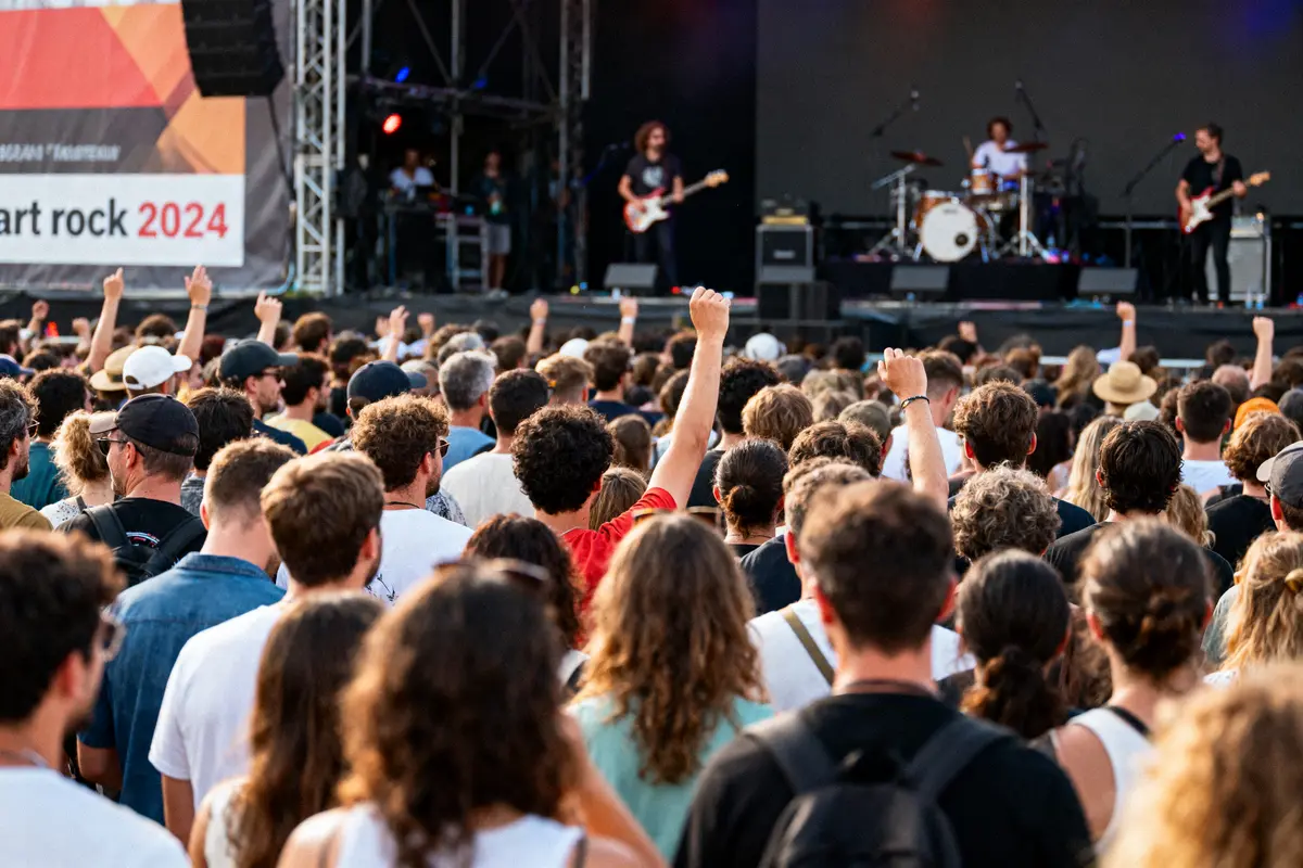 Foule enthousiaste lors d'un concert extérieur avec un groupe sur scène, pancarte "Art Rock 2024".