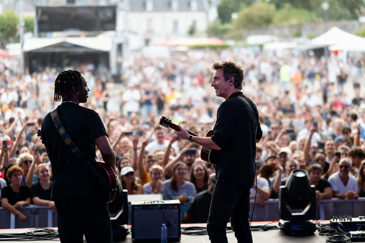 Deux musiciens jouent sur scène devant une foule enthousiaste lors d'un concert en plein air.