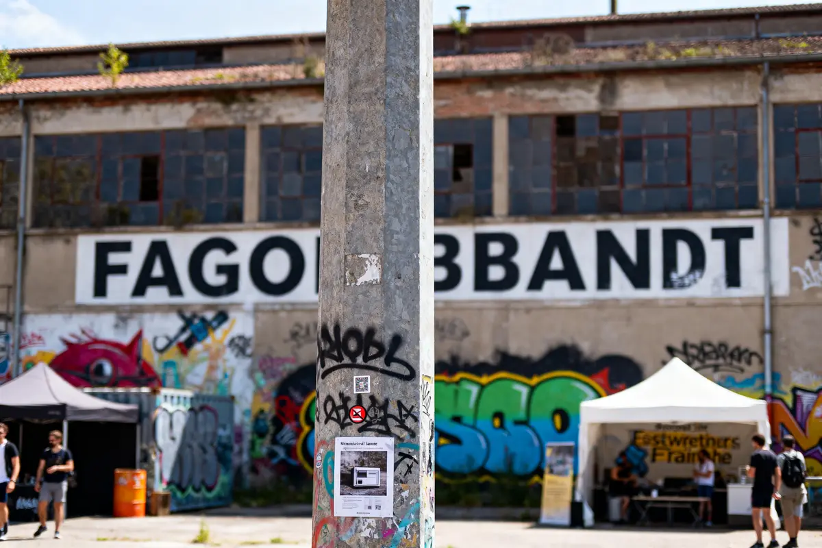 Bâtiment industriel abandonné avec graffiti, grande enseigne FAGO BABBANDT, tente blanche, pilier tagué au premier plan.