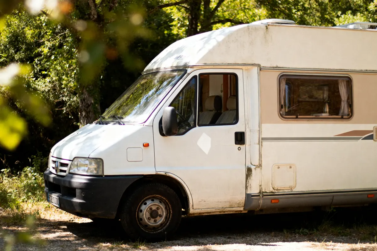 Camping-car blanc garé en plein air, entouré d'arbres verdoyants, par une journée ensoleillée.