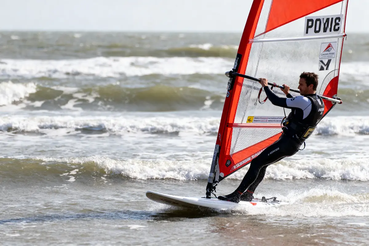 Personne pratiquant la planche à voile sur la mer agitée, sous un ciel dégagé.